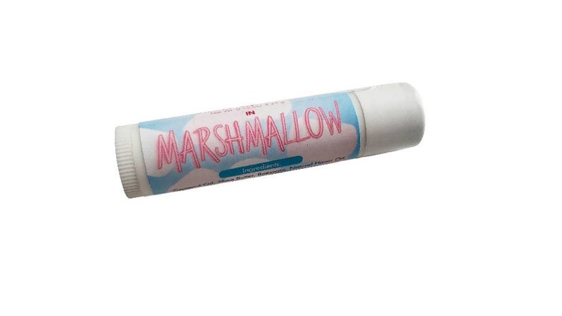 May include: A cylindrical lip balm tube with a white cap and a light blue label featuring a white cloud pattern. The text MARSHMALLOW is printed in large pink letters across the center of the label, with smaller text listing ingredients below.