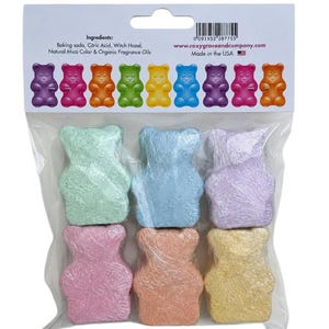 A clear plastic bag contains six individually wrapped colorful bear-shaped bath bombs below a cardboard header listing ingredients and website details.