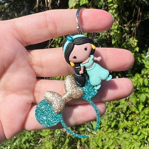 May include: Teal blue and gold glitter Minnie Mouse ears with a small, teal blue and gold glitter Jasmine figurine attached.