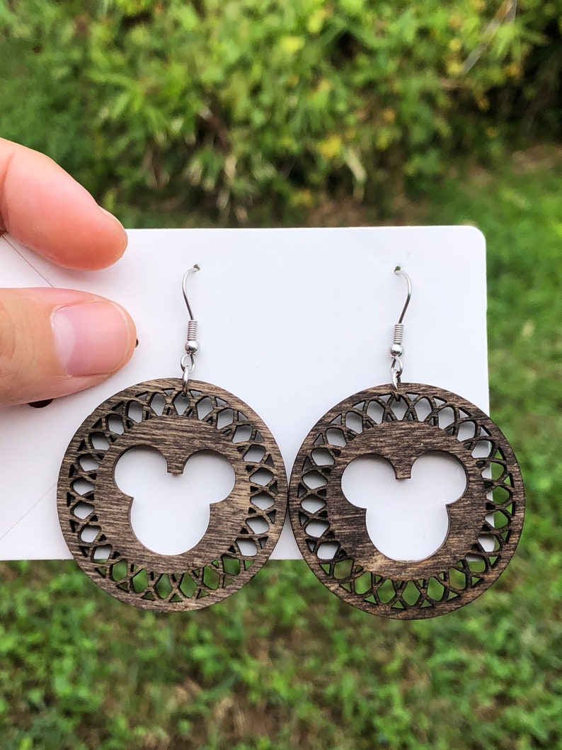May include: Wooden dangle earrings featuring a dark brown circular design with a Mickey Mouse silhouette in the center. The earrings have a decorative openwork pattern around the mouse head and silver-colored ear wires.