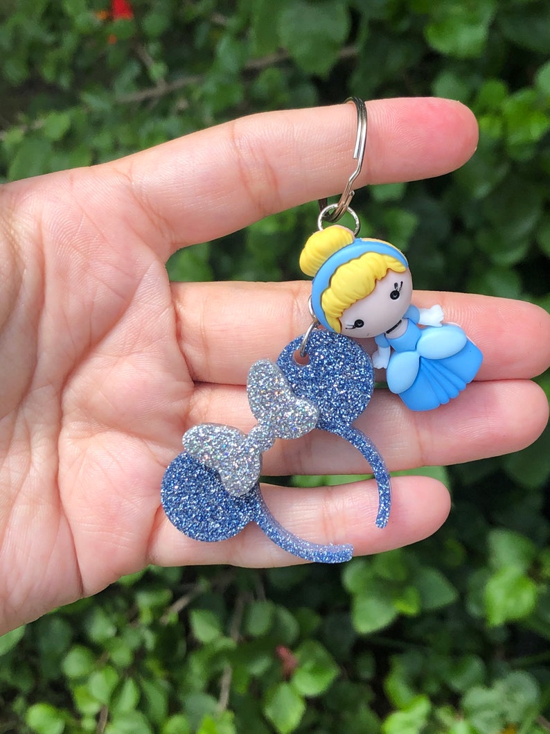 May include: Blue glitter Minnie Mouse ears with a silver bow and a blue and white Cinderella charm attached to a silver key chain.