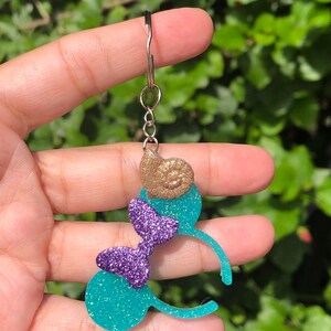 May include: Teal and purple glitter Minnie Mouse ears with a gold seashell charm attached to a silver key chain.