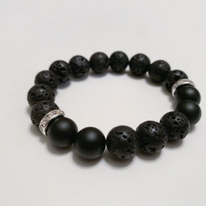 Puede incluir: Pulsera de cuentas negras con una combinación de cuentas de ónix mate y piedra de lava texturizada. La pulsera incluye dos espaciadores plateados con detalles de cristal transparente. Un accesorio elegante. Circunferencia de unos 19 cm.