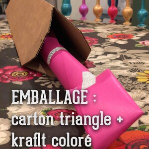 Puede incluir: Un tri&aacute;ngulo de cart&oacute;n rosa con el texto "EMBALLAGE : carton triangle + kraft color&eacute;" est&aacute; envuelto alrededor de un tubo rosa con purpurina plateada.