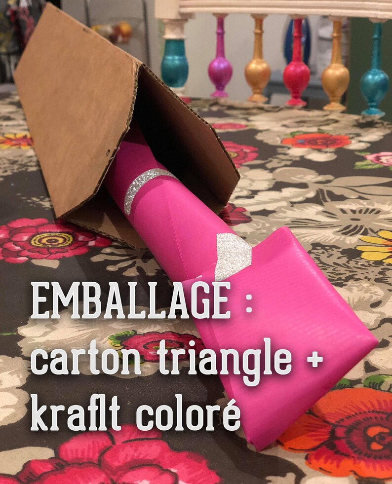 Puede incluir: Un tri&aacute;ngulo de cart&oacute;n rosa con el texto "EMBALLAGE : carton triangle + kraft color&eacute;" est&aacute; envuelto alrededor de un tubo rosa con purpurina plateada.