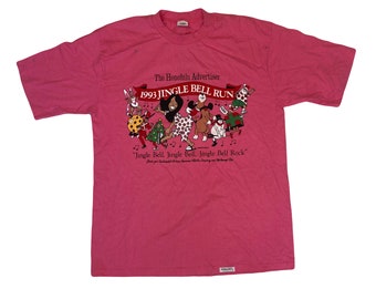 Puede incluir: Camiseta rosa con un gráfico de personajes de dibujos animados celebrando la carrera Jingle Bell Run de 1993. El Honolulu Advertiser está impreso en la camiseta. El texto "Jingle Bell, Jingle Bell, Jingle Bell Rock" está impreso en la camiseta.
