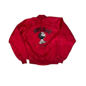 May include: A red satin bomber jacket with a black and white graphic on the back. The graphic features a cartoon eight-ball character wearing sneakers, with the text "RUBY'S PLACE" above it. Additional text is below the graphic.