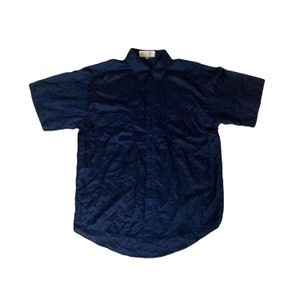 以下が含まれることがあります： テクスチャのある生地のネイビーブルーの半袖ボタンダウンシャツ。シャツは胸に2つのポケットとボタンダウンカラーが付いています。