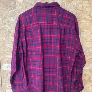 May include: A red and black checked flannel shirt with long sleeves and a button-up front.