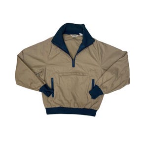 Puede incluir: Chaqueta tipo jersey de color beige con cuello, puños y dobladillo azul marino. La chaqueta presenta un cierre de cremallera de un cuarto, un bolsillo delantero y detalles en azul marino en las mangas. Fabricada con un material ligero.