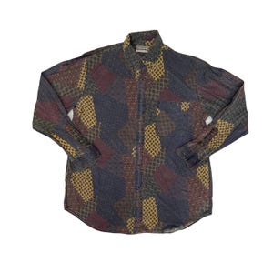 Peut inclure: Chemise boutonnée à manches longues avec un motif patchwork dans les tons bleu marine, bordeaux et jaune moutarde. La chemise a un col et une poche poitrine unique. Le tissu a un aspect légèrement texturé.