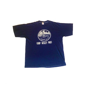 May include: A navy blue t-shirt with a white graphic of a city skyline and the text "Camp Wesley Pines".