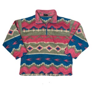 May include: A fleece pullover with a colorful geometric pattern. The design features pink, teal, and gray shapes. The collar and zipper are teal. The pullover has long sleeves and a relaxed fit.