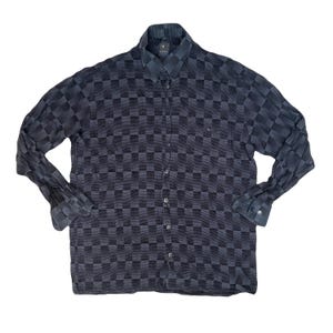 Puede incluir: Una camisa de manga larga con un estampado a cuadros azul oscuro y gris. La camisa tiene un cuello clásico y puños abotonados. La tela parece ligera.