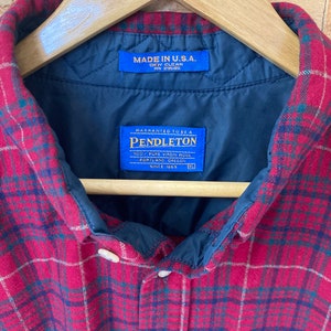 May include: Red and black plaid flannel shirt with a blue label that reads "Made in U.S.A. Dry Clean RN 29605" and a blue label that reads "Warranted to be a Pendleton 100% Pure Virgin Wool Portland, Oregon Since 1869".