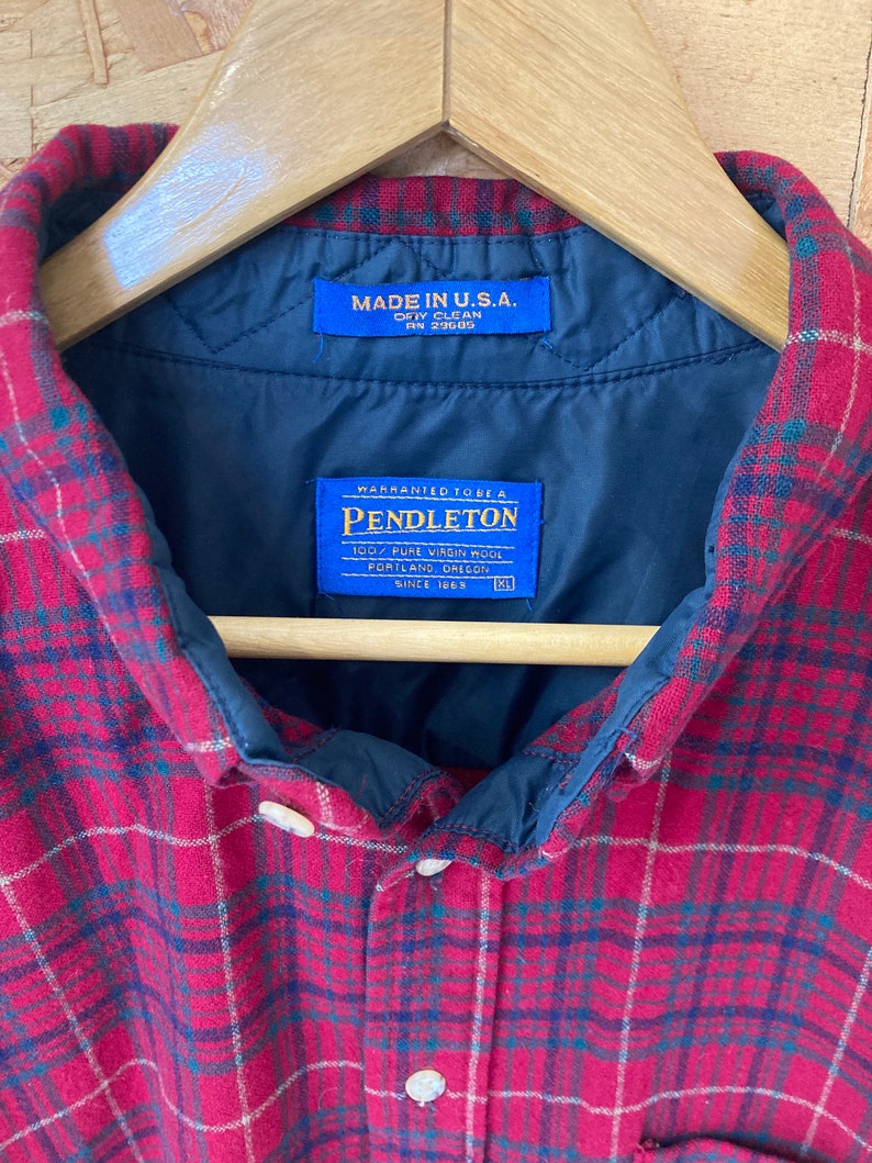 May include: Red and black plaid flannel shirt with a blue label that reads "Made in U.S.A. Dry Clean RN 29605" and a blue label that reads "Warranted to be a Pendleton 100% Pure Virgin Wool Portland, Oregon Since 1869".