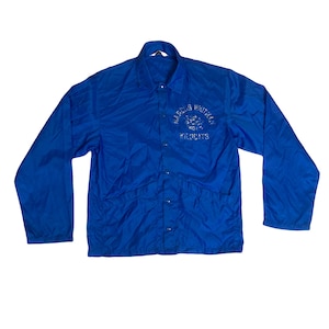 Könnte beinhalten: Eine leuchtend blaue Vintage-Jacke mit langen Ärmeln und Knopfleiste. Auf der Jacke steht der Text "MARCUS WHITMAN" über einer Wildkatzen-Grafik und das Wort "WILDCATS" in Weiß. Zwei Taschen sind sichtbar.