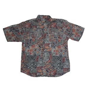 Puede incluir: Una camisa de manga corta con botones y un patrón geométrico en tonos marrones, grises y naranjas.