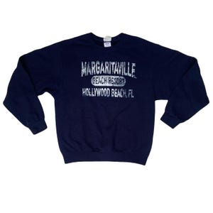 Può includere: Felpa blu navy con la scritta "MARGARITAVILLE BEACH RESORT HOLLYWOOD BEACH, FL" in lettere bianche sbiadite. Il top a girocollo a maniche lunghe è uno stile casual.