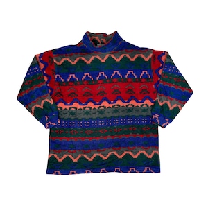 May include: A vintage fleece pullover with a high neck and long sleeves. The sweater has a colourful geometric pattern in red, blue, green, grey, and peach. The design is a repeating pattern of zigzags and other shapes.