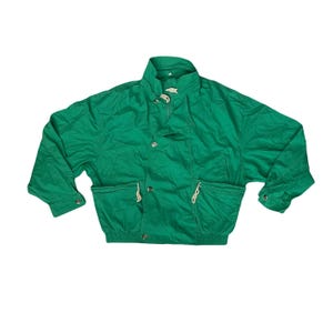 May include: A vibrant green jacket featuring a high collar, button fastenings, and two front pockets. The jacket has long sleeves with buttoned cuffs and drawstring details. The fabric appears lightweight and slightly creased, suggesting a casual style.