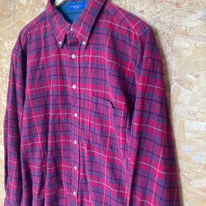 May include: Red and black plaid flannel shirt with a button-down collar and a single chest pocket. The shirt has a "Made in USA" tag.