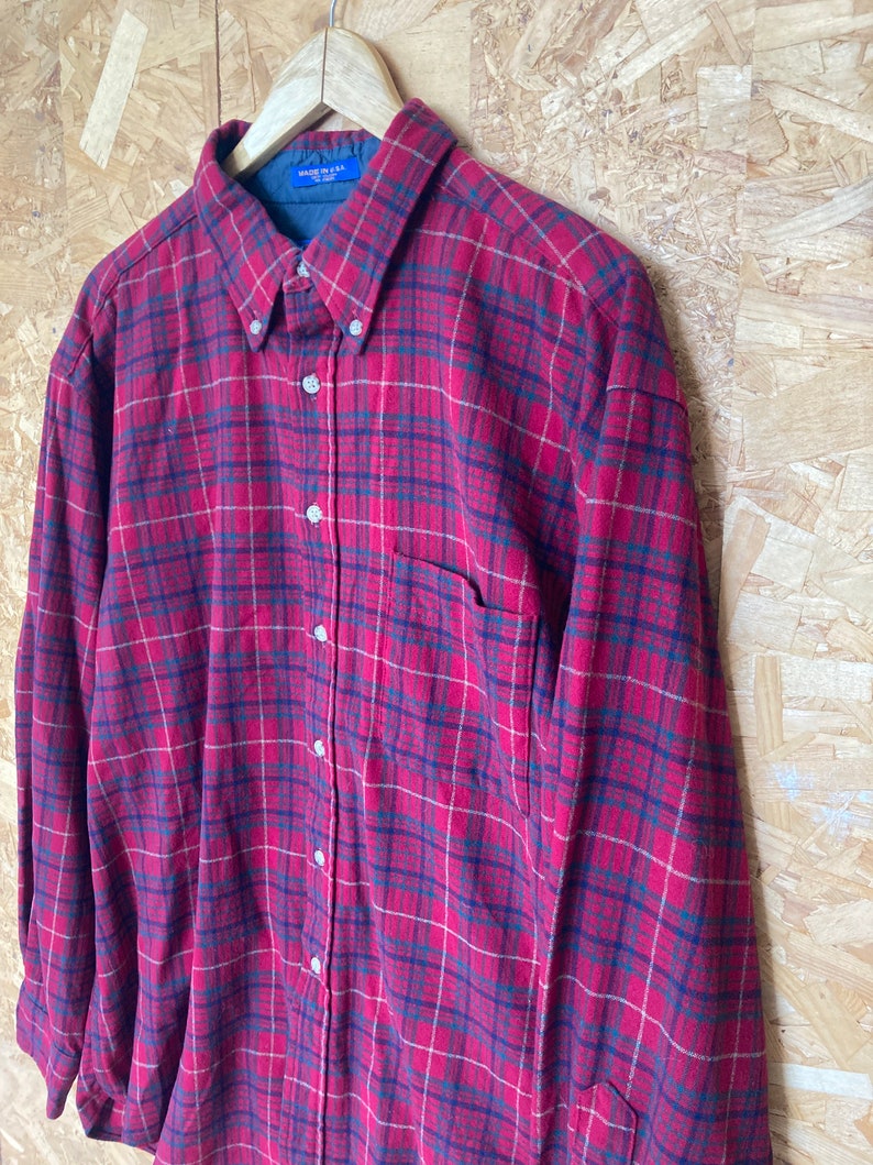 May include: Red and black plaid flannel shirt with a button-down collar and a single chest pocket. The shirt has a "Made in USA" tag.