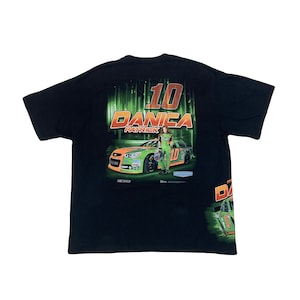Pode incluir: Camiseta preta com um gráfico verde e laranja de um carro de corrida e um piloto. O texto "10 Danica Patrick" está impresso na camiseta.
