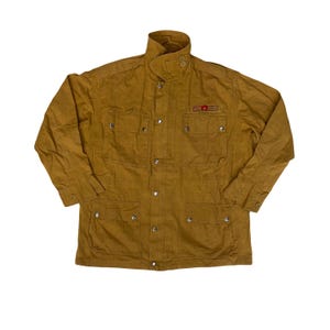 May include: Mustard-coloured jacket with a high collar and multiple pockets. The jacket features a button-up front and a small red and gold emblem on the chest. The jacket is made of a durable fabric and has a classic, utilitarian design.