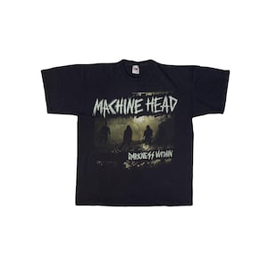 Puede incluir: Camiseta negra de Machine Head con el nombre de la banda en blanco, letras estilizadas sobre un gráfico de figuras silueteadas. El texto "DARKNESS WITHIN" está debajo. Cuello redondo clásico.