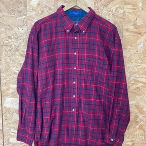 May include: A red, black and white plaid long-sleeved button-down shirt. The shirt has a single chest pocket and is made in the U.S.A.