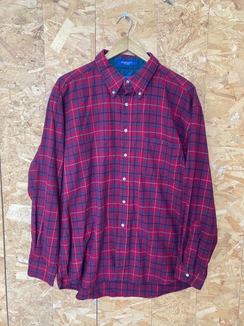 May include: A red, black and white plaid long-sleeved button-down shirt. The shirt has a single chest pocket and is made in the U.S.A.