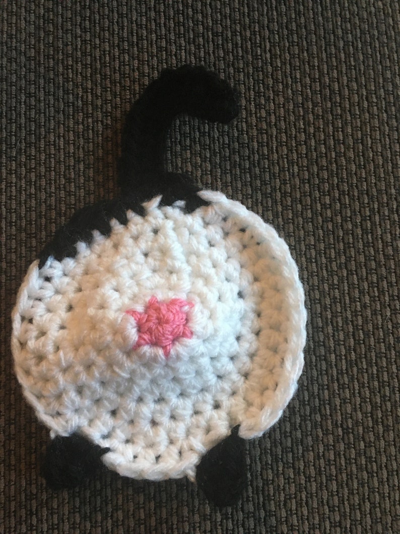 Puede incluir: Un gato de crochet blanco con orejas, cola y patas negras. El gato tiene una nariz rosa.