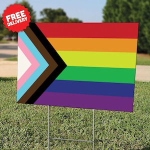 May include: A yard sign featuring a pride flag with a black and brown chevron on a white background, followed by the colors of the rainbow: red, orange, yellow, green, blue, and purple.