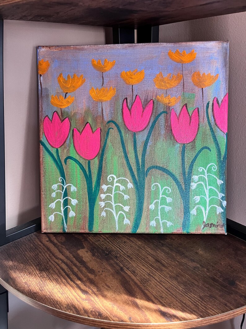May include: A painting of a field of pink and orange flowers. The flowers are painted in a simple, stylized way. The background is a light blue with hints of green and purple. The painting is signed "Jami" in the bottom right corner.