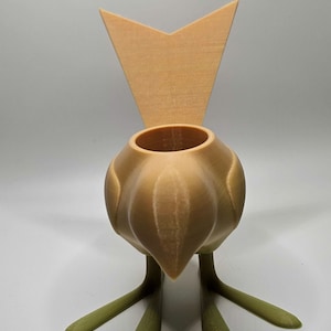 May include: A 3D printed bird-shaped planter with a light brown body and green legs. The planter has a small opening at the top for planting.