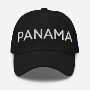 Può includere: Un cappello da baseball nero con testo ricamato in bianco che dice "PANAMA". Il cappello ha una piccola bandiera blu e bianca sul lato.