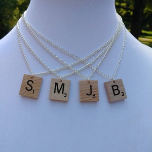May include: Four silver necklaces with wooden Scrabble tile pendants spelling out the letters "S1", "M3", "J8", and "B3".