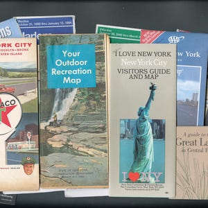 May include: A collection of vintage New York City travel brochures and maps, including a Texaco road map, a New York State outdoor recreation map, an I Love New York visitors guide featuring the Statue of Liberty, and a guide to the Great Lawn.