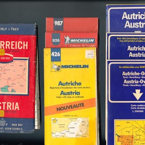 May include: A collection of five vintage road maps of Austria, featuring the Michelin brand and the text "Austria" in both German and English. The maps are in various colors, including blue, red, yellow, and white.