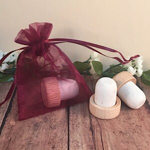 May include: Two white bottle stoppers with wooden bases, one in a burgundy organza bag. The stoppers are made of cork and have a natural finish.