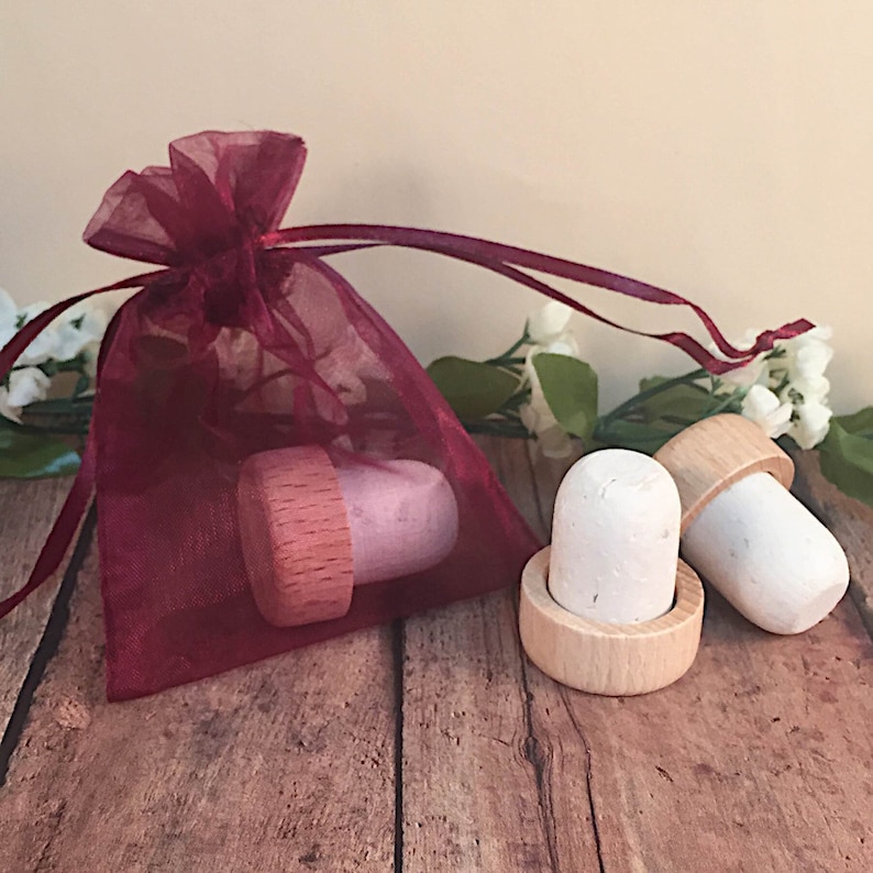 May include: Two white bottle stoppers with wooden bases, one in a burgundy organza bag. The stoppers are made of cork and have a natural finish.