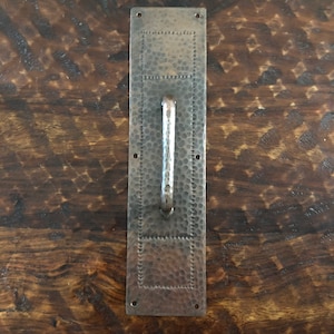 以下が含まれることがあります： 長方形のバックプレートと湾曲した金属製のハンドルが付いた、ハンマーで叩かれた銅製のドアハンドルです。