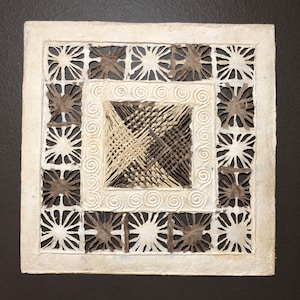 May include: A white paper square with a brown paper design. The design is a series of concentric squares with a woven pattern in the center.