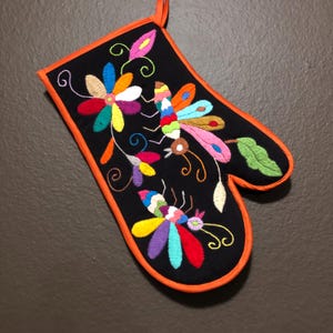May include: Black oven mitt with an orange trim and colorful embroidered butterflies and flowers.
