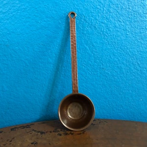 Könnte beinhalten: Eine gehämmerte Kupfer Schöpfkelle mit einem langen Stiel und einer abgerundeten Schüssel. Die Schöpfkelle ist ein Küchenutensilien zum Servieren von Flüssigkeiten.