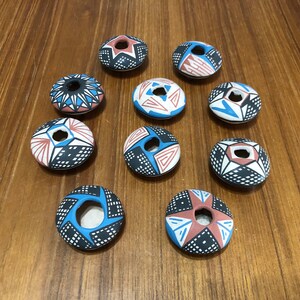 May include: Ten small, round, ceramic trinket dishes with a variety of geometric patterns in blue, red, and white. The dishes have a small hole in the center.