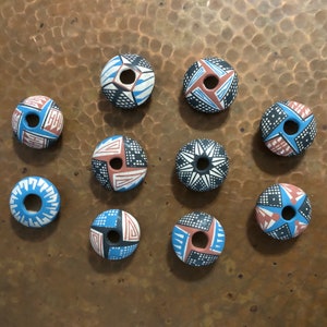 May include: Ten ceramic round beads with a hole in the center. Each bead is painted with a different geometric pattern in shades of blue, red, black, and white.