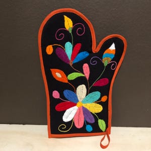 May include: Black oven mitt with a colorful floral embroidery design. The mitt has an orange trim and a hanging loop.
