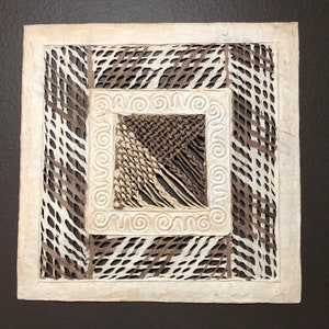 May include: A square, white paper artwork with a brown paper design. The artwork features a woven pattern in the center, surrounded by a decorative border.